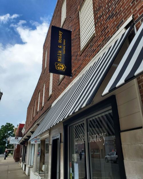 Exterior of a brick building with a striped awning and a sign for "milk & honey" hanging above the entrance.