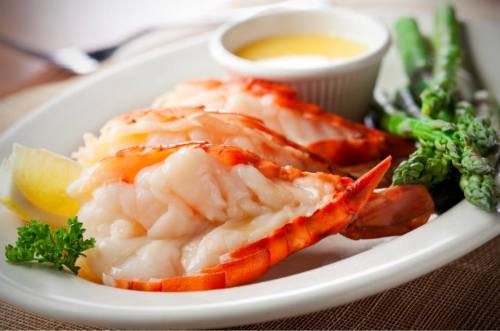 A plate of shrimp with lemon, asparagus, and a small bowl of dipping sauce.
