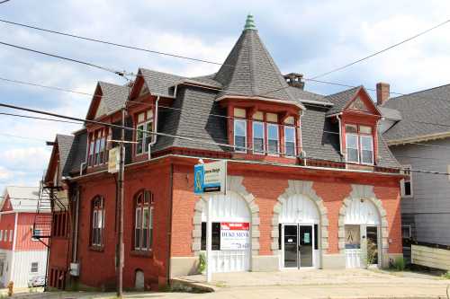 Historic red brick building with arched windows, featuring a "For Sale" sign and a distinctive roofline.