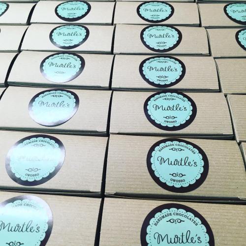Rows of brown boxes with teal labels reading "Murtle's Handmade Chocolates, Owosso."