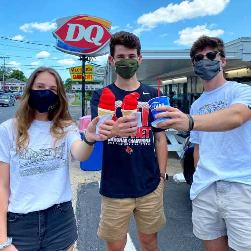 Three friends wearing masks hold ice cream treats outside a Dairy Queen on a sunny day.