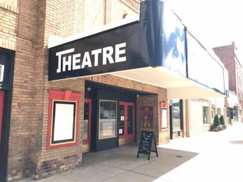 A brick building with a marquee sign reading "THEATRE" and a chalkboard menu outside.
