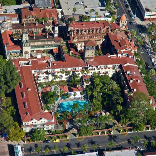 Aerial view of a large, lush hotel complex with red roofs, a central pool, and surrounding palm trees.