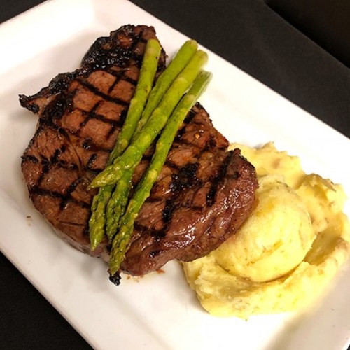 Grilled steak with asparagus and creamy mashed potatoes on a white plate.