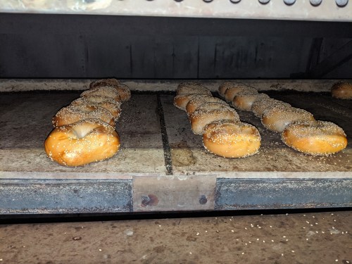 Freshly baked bagels with sesame seeds cooling on a rack in an oven.