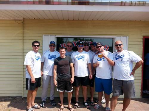 A group of eight men in matching shirts pose together outside a restaurant, smiling and enjoying their time.