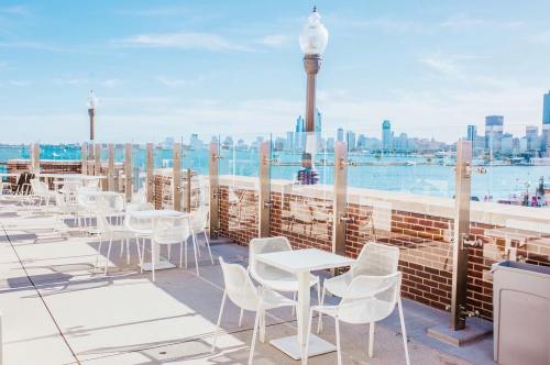 A sunny outdoor terrace with white chairs and tables, overlooking a city skyline and waterfront.