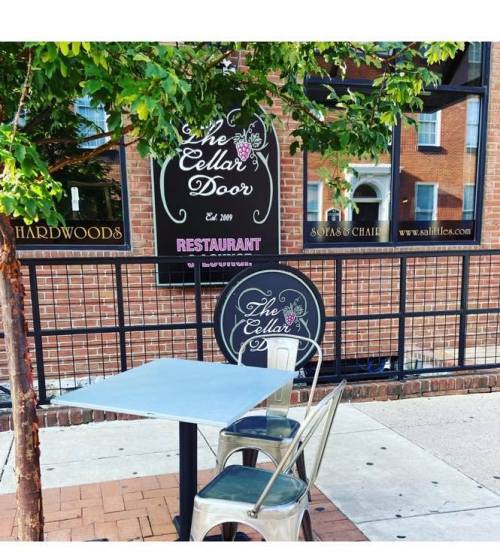 A small outdoor dining area with a metal table and chair in front of "The Cellar Door" restaurant sign.