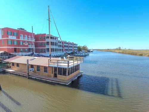 A wooden boat house on a calm waterway, with colorful buildings in the background under a clear blue sky.