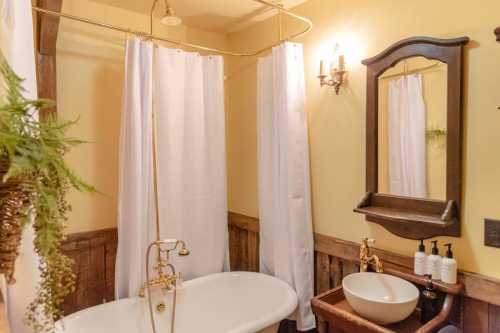 A cozy bathroom featuring a freestanding tub, shower curtains, a wooden mirror, and a stylish sink.