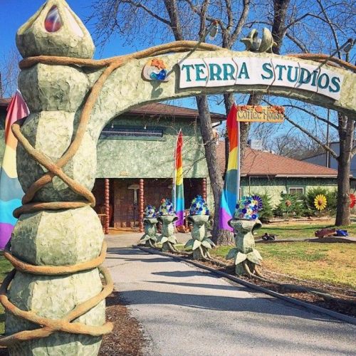 Entrance to Terra Studios, featuring a whimsical arch and colorful flags, surrounded by artistic sculptures.