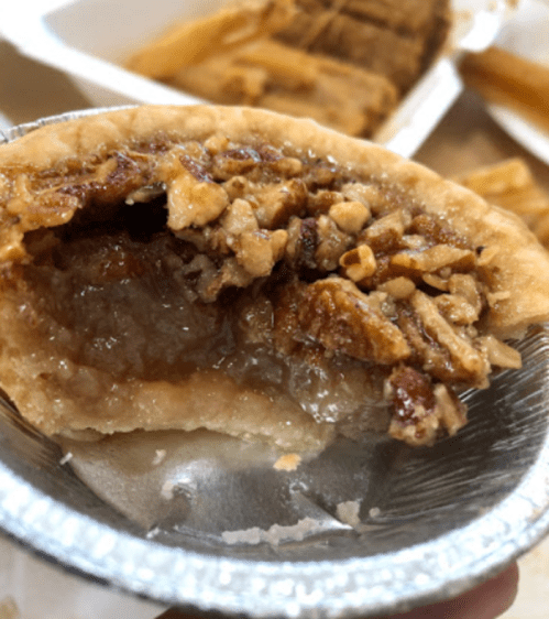 Close-up of a pecan pie slice with a flaky crust and a gooey filling, showcasing nuts and a shiny surface.