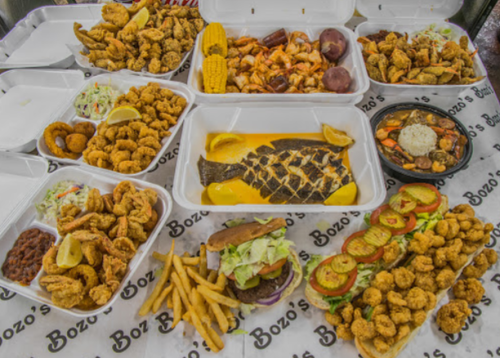 A variety of seafood dishes including fried shrimp, fish, and sides, arranged in takeout containers on a table.
