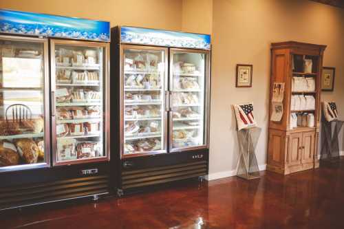 Two glass-fronted freezers filled with packaged food items, alongside a wooden display cabinet with documents and an American flag.