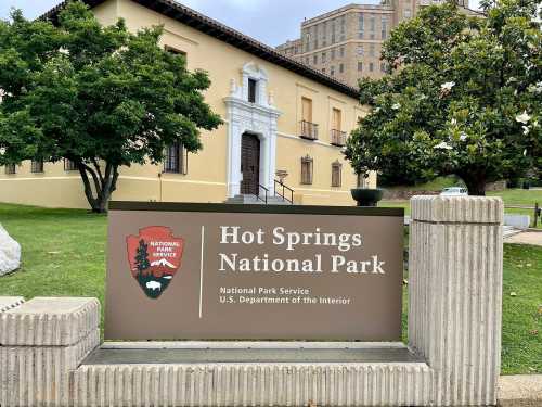 Sign for Hot Springs National Park, featuring the National Park Service logo and a historic building in the background.