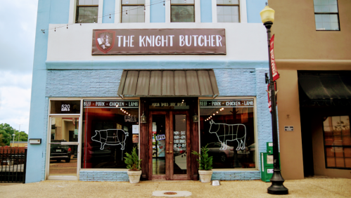 Exterior of "The Knight Butcher" shop, featuring a blue facade and large windows with animal illustrations.