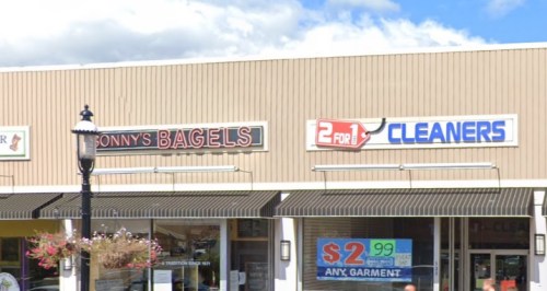 Signage for "Sonny's Bagels" and "2 for 1 Cleaners" on a storefront, with a lamp post and flower baskets in view.