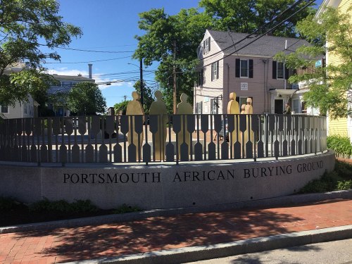 A memorial with silhouettes representing figures, marking the Portsmouth African Burying Ground, surrounded by greenery.