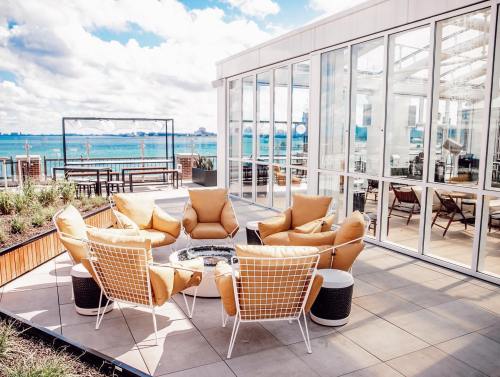 A cozy outdoor seating area with yellow chairs around a fire pit, overlooking a waterfront view and blue sky.