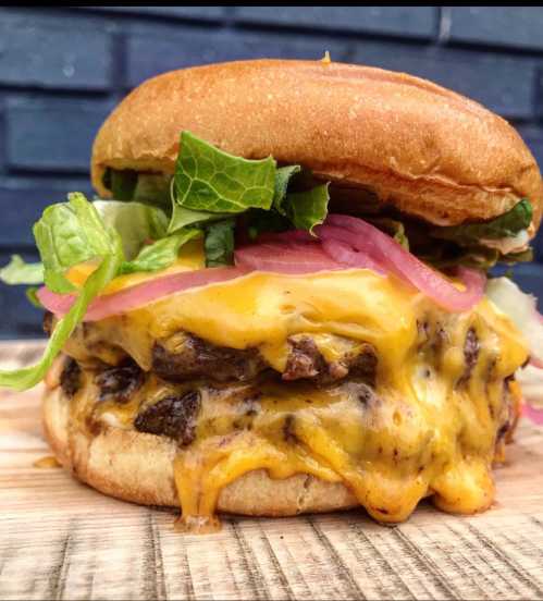 A juicy cheeseburger with melted cheese, lettuce, pickled onions, and a toasted bun, served on a wooden board.