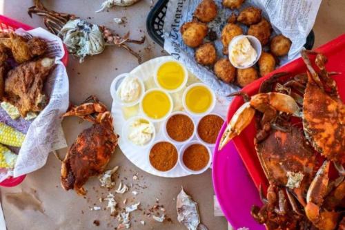 A spread of seafood featuring crabs, fried food, and dipping sauces on a table covered with brown paper.