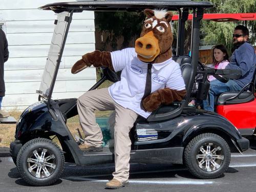 A person in a horse costume sits in a golf cart, wearing a white shirt and posing playfully.
