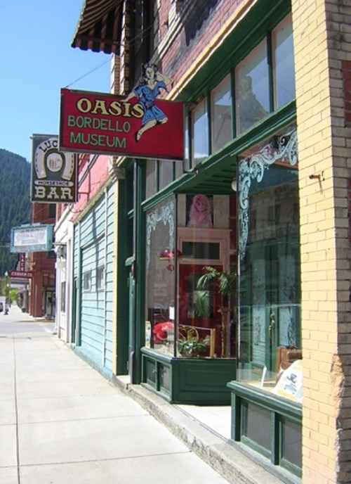 Exterior of the Oasis Bordello Museum, featuring a colorful sign and large windows displaying various items inside.