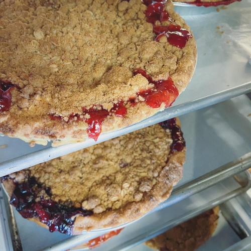 Two freshly baked pies on a cooling rack, one with a crumbly topping and cherry filling, the other with a darker filling.