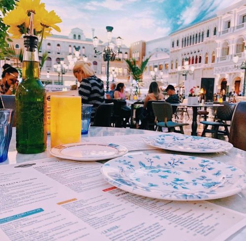 A table set with empty plates, a drink, and a menu, surrounded by a lively outdoor dining area.
