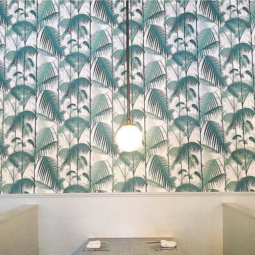 A stylish interior featuring a palm leaf patterned wallpaper and a round pendant light hanging above a table.