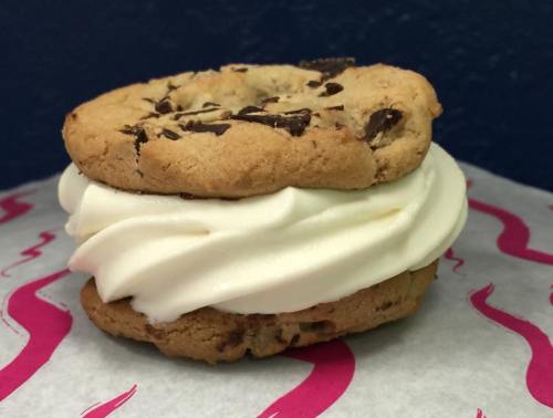 A delicious cookie sandwich with chocolate chips and creamy vanilla ice cream in the middle, resting on pink patterned paper.
