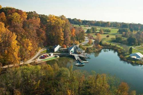Aerial view of a serene lakeside scene with autumn foliage, a dock, and boats near a charming building.