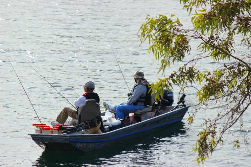 Two fishermen in a small boat, casting lines into a calm lake surrounded by greenery.