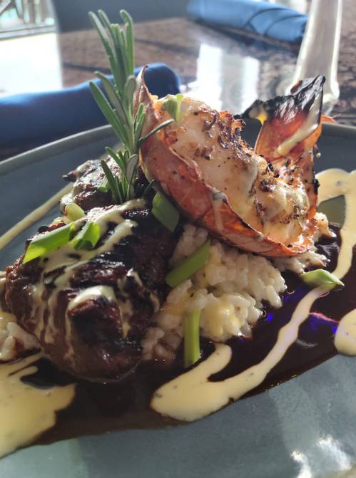 A gourmet dish featuring grilled shrimp on risotto, garnished with rosemary and drizzled with sauce.