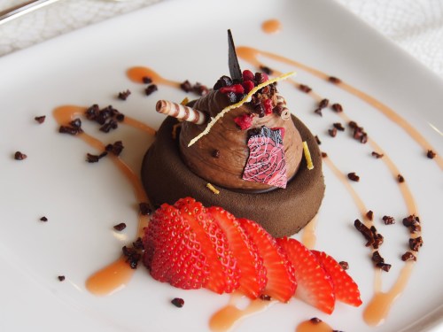 A chocolate dessert topped with a decorative piece, surrounded by strawberry slices and drizzled with sauce.