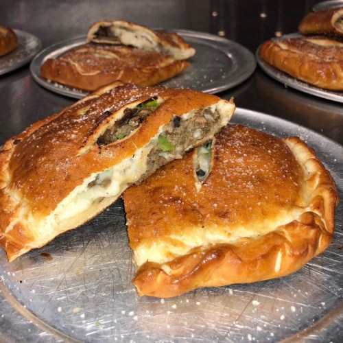 A close-up of a golden-brown pastry, split open to reveal a savory filling of meat and vegetables.