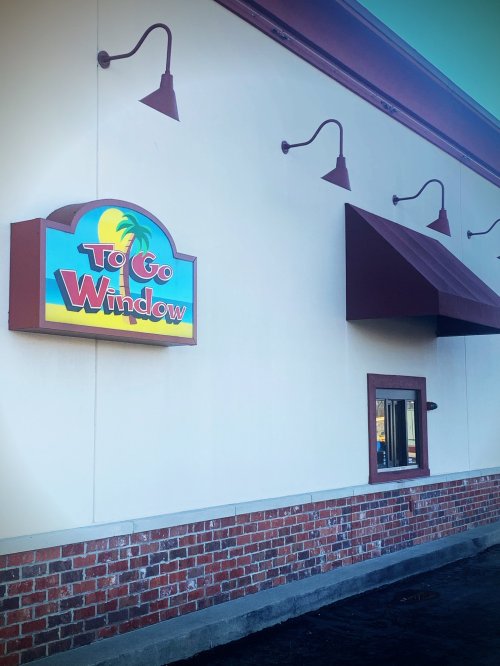 A colorful sign reading "To Go Window" on a restaurant exterior with a brown awning and brick base.
