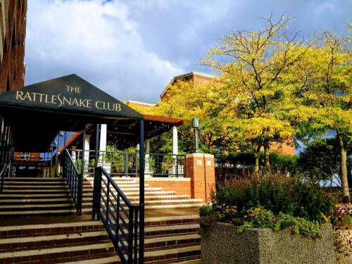 Entrance to The Rattlesnake Club with stairs, colorful foliage, and a cloudy sky in the background.