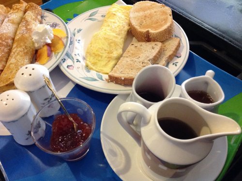 A breakfast plate with pancakes, an omelet, toast, jam, and coffee served on a colorful tray.