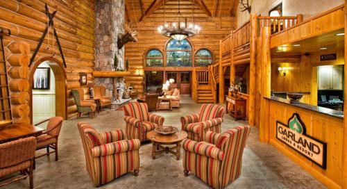 Cozy lodge interior with wooden walls, stone accents, and striped chairs around a central table. Garland Lake Resort sign visible.