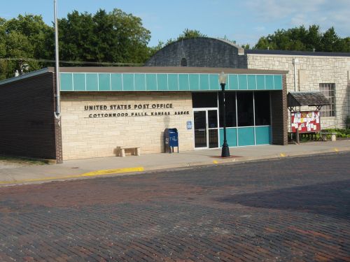Exterior of the United States Post Office in Cottonwood Falls, Kansas, featuring a brick sidewalk and clear blue sky.