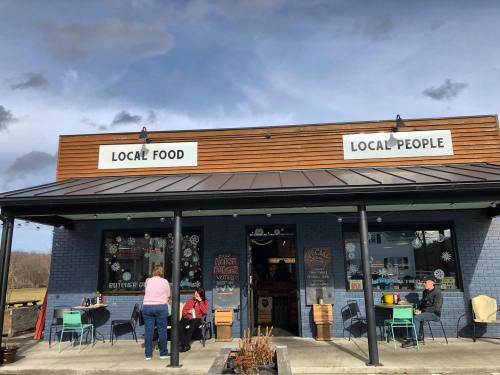 A cozy restaurant exterior with signs reading "Local Food" and "Local People," featuring outdoor seating and patrons.