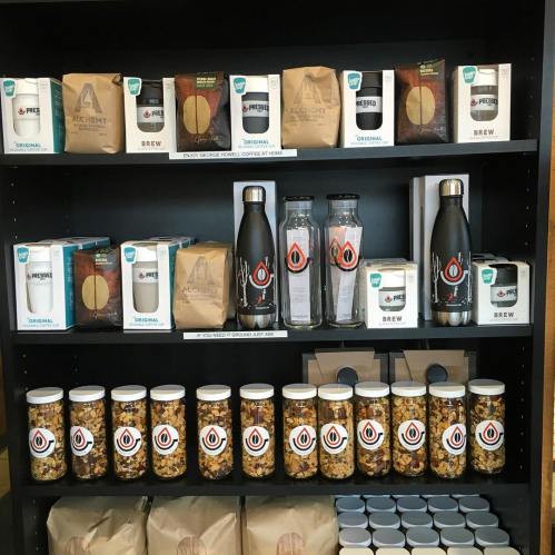 A shelf displaying various coffee products, water bottles, and snacks in jars, all neatly arranged.