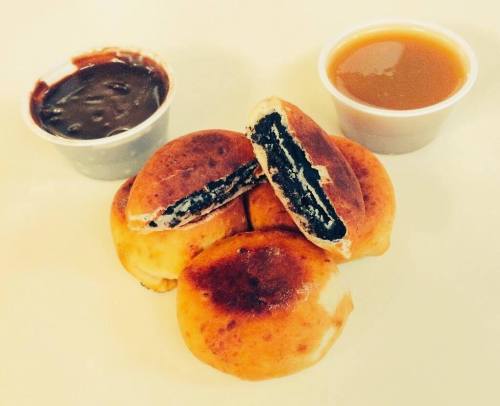 A stack of golden-brown stuffed pastries with a chocolate filling, accompanied by two dipping sauces.