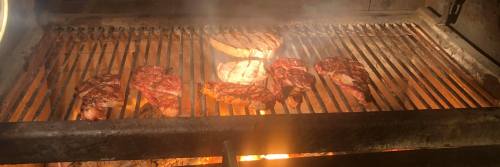 Grilling various cuts of meat on a barbecue, with flames and smoke rising from the grill.