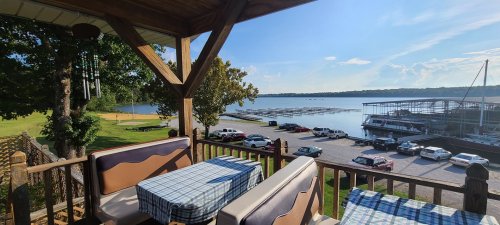 View from a deck overlooking a lake with boats, parked cars, and a clear blue sky.
