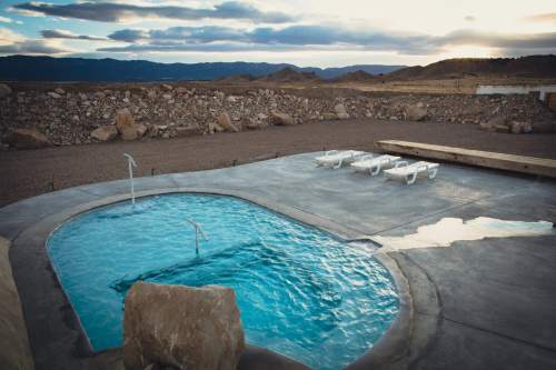 A serene outdoor hot tub surrounded by rocky terrain and lounge chairs, with mountains in the background under a cloudy sky.