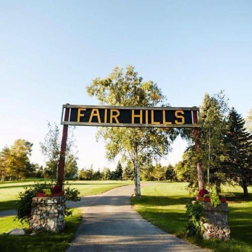 Sign reading "Fair Hills" at the entrance of a scenic pathway surrounded by trees and greenery.