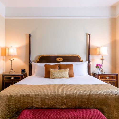 Cozy hotel room featuring a queen bed, decorative pillows, bedside lamps, and elegant furnishings.