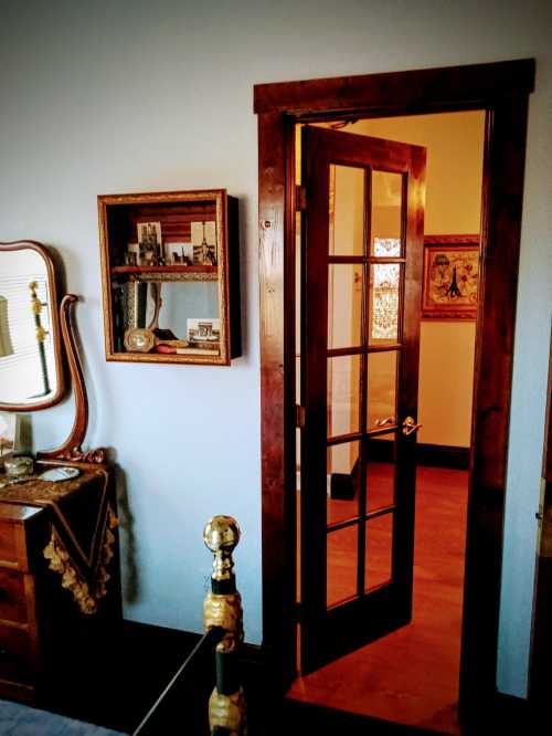 A wooden door opens into a room, revealing a vintage decor with a mirror and framed pictures on the wall.